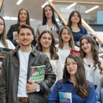 Diverse group of students smiling on stairs, holding educational books indoors.