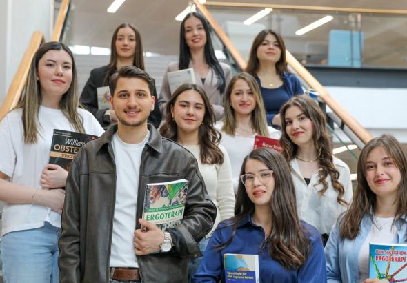 Diverse group of students smiling on stairs, holding educational books indoors.